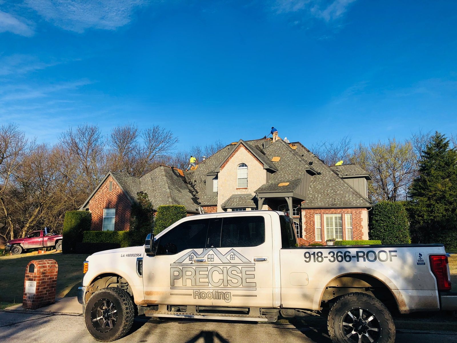 Precise Roofing truck parked in front of a home with the crew on the roof